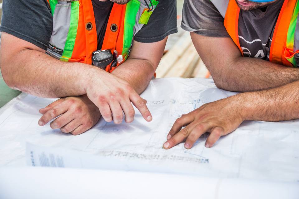 Two crew members in safety vests reviewing construction plans